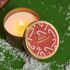 Свічка Xmas Candle Winter Clementine: запалена свічка в жерстяній банці з кришкою з льодяниками
