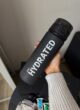 Спортивна пляшка для води 700 мл, чорна матова з написом STAY HYDRATED у руці
