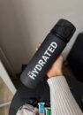 Спортивна пляшка для води 700 мл, чорна матова з написом STAY HYDRATED у руці