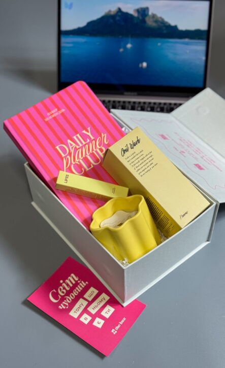 Бокс SUNNY GIRL: біла коробка з планером Daily Planner Club, жовтою свічкою та бальзамом LIPSS біля ноутбука