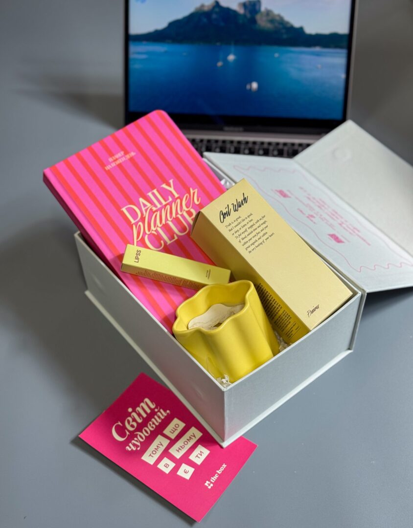 Бокс SUNNY GIRL: біла коробка з планером Daily Planner Club, жовтою свічкою та бальзамом LIPSS біля ноутбука