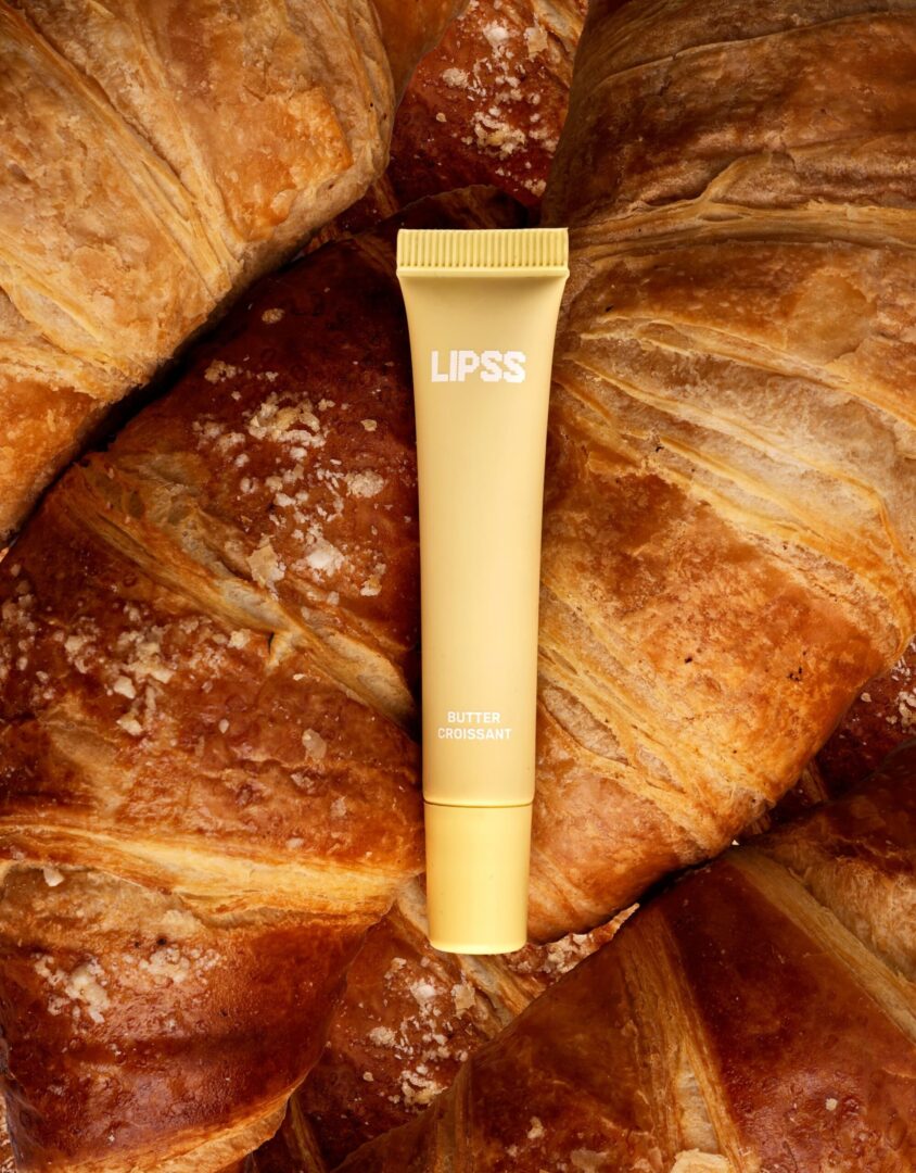 Блиск для губ LIPSS Butter Croissant 8 мл: жовта туба лежить на свіжих круасанах