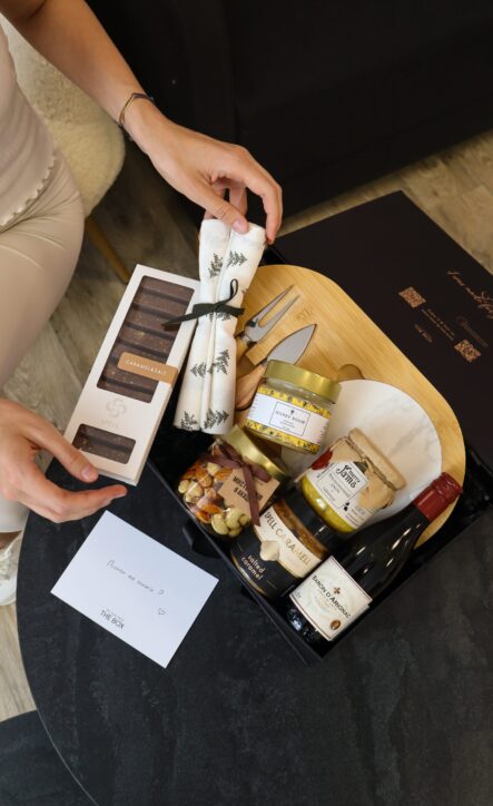 Бокс CHEESE LOVER: жінка розпаковує чорну коробку з бамбуковою дошкою, ножами для сиру, медом, горіхами та вином