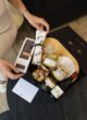 Бокс CHEESE LOVER: жінка розпаковує чорну коробку з бамбуковою дошкою, ножами для сиру, медом, горіхами та вином
