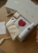 CUPID LOVE: коробка THE BOX збоку з білою стрічкою, шкарпетками, маскою та піною Rituals