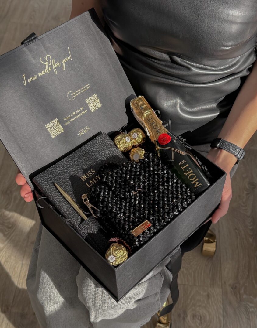 Бокс ELEGANCE у руках жінки в сріблястій сукні: чорна сумка з кристалів, Moët, цукерки Ferrero Rocher та ручка